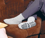 Graue Stricksocken mit ABS-Anti-Rutschsohle „STOP“, getragen auf einem Sofa.