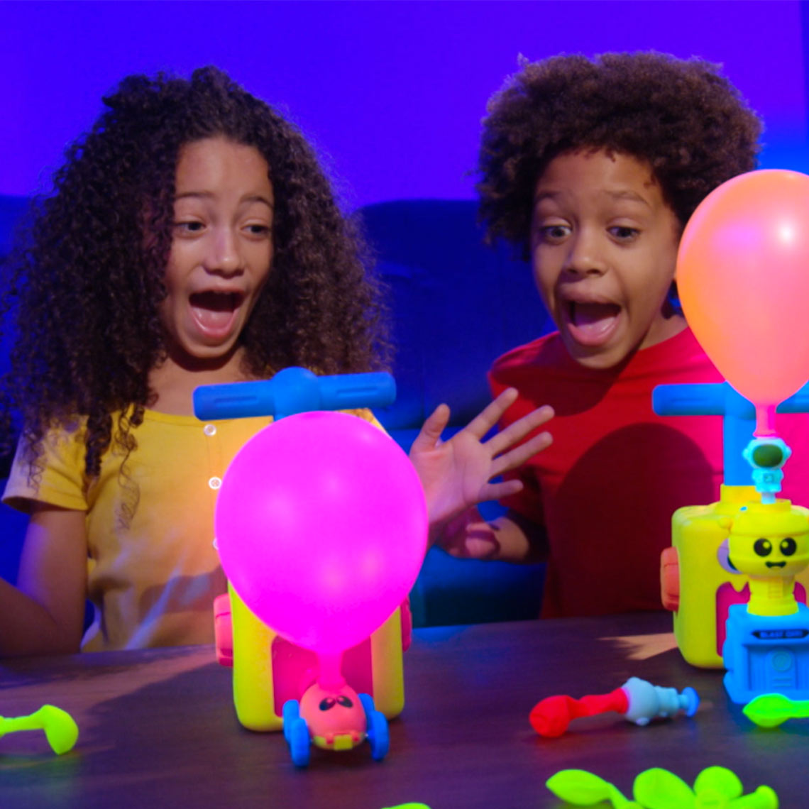 Zwei Kinder spielen begeistert mit dem farbenfrohen Balloon Zoom und beobachten aufblasende Ballons.