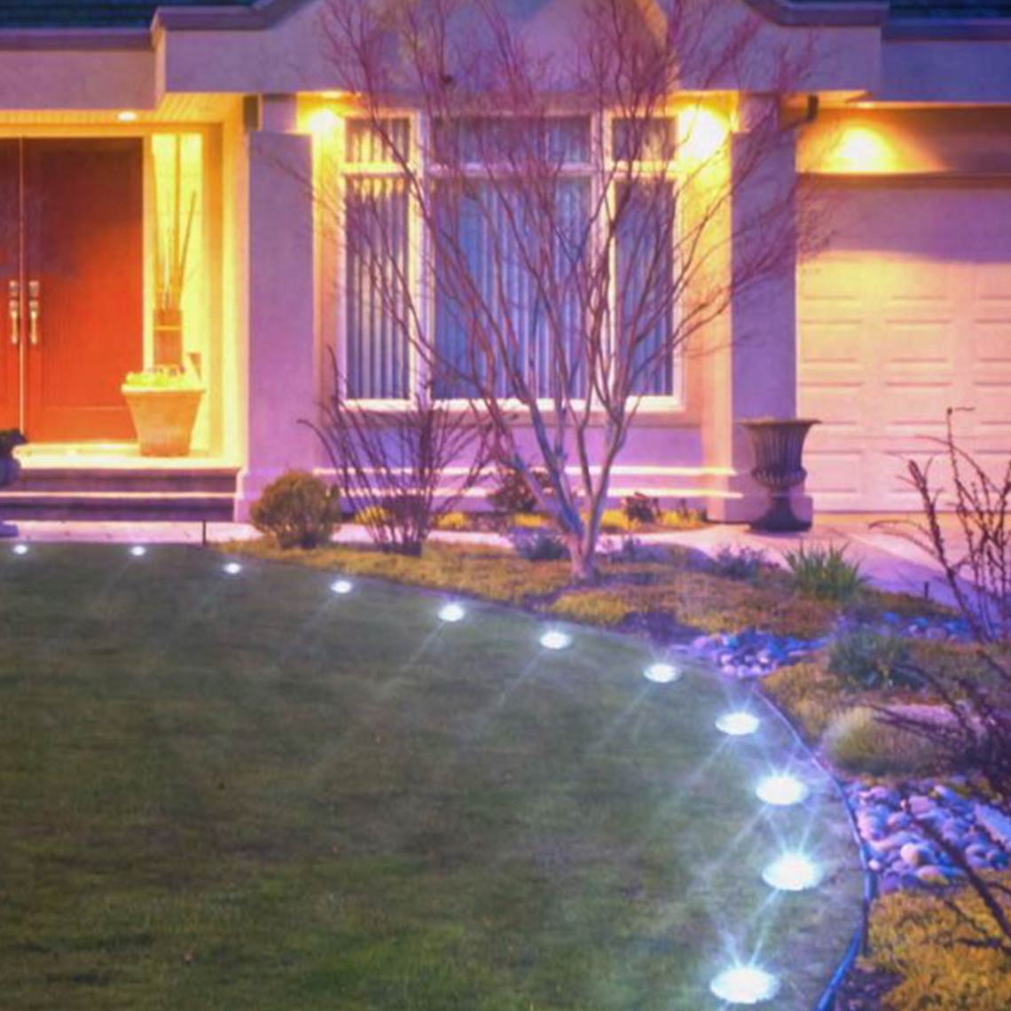 Beleuchteter Gartenweg mit kreisförmig angeordneten Disk Lights Stone Leuchten entlang der Rasenfläche.
