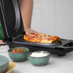 Gefüllte Enchiladas mit Sauce und Käse in einem kompakten Livington CleverChef Multicooker, daneben Schälchen mit Salsa und Sauerrahm.