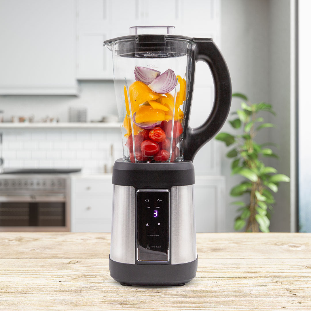 Moderner Standmixer auf einer Küchenarbeitsfläche, gefüllt mit frischen Zutaten wie gelber Paprika, roten Tomaten und roten Zwiebelstücken.