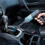 Mit einem Handstaubsauger reinigt eine Person den Innenraum des Autos rund um die Gangschaltung.