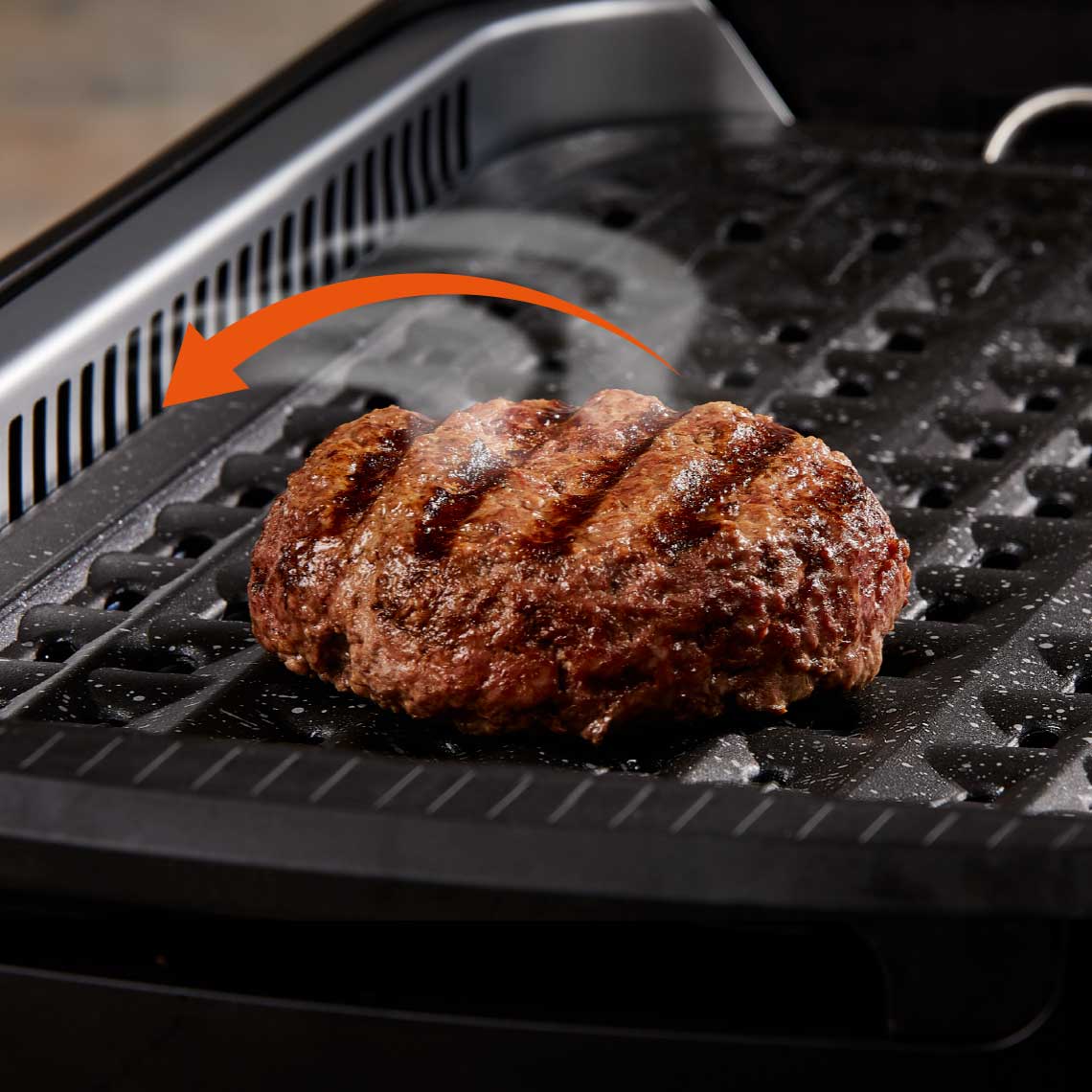 PowerXL Smokeless Grill – saftiger Burger auf gerillter Platte, mit Pfeil zur Rauchabzugsfunktion.