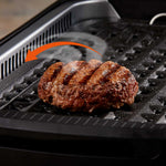PowerXL Smokeless Grill – saftiger Burger auf gerillter Platte, mit Pfeil zur Rauchabzugsfunktion.