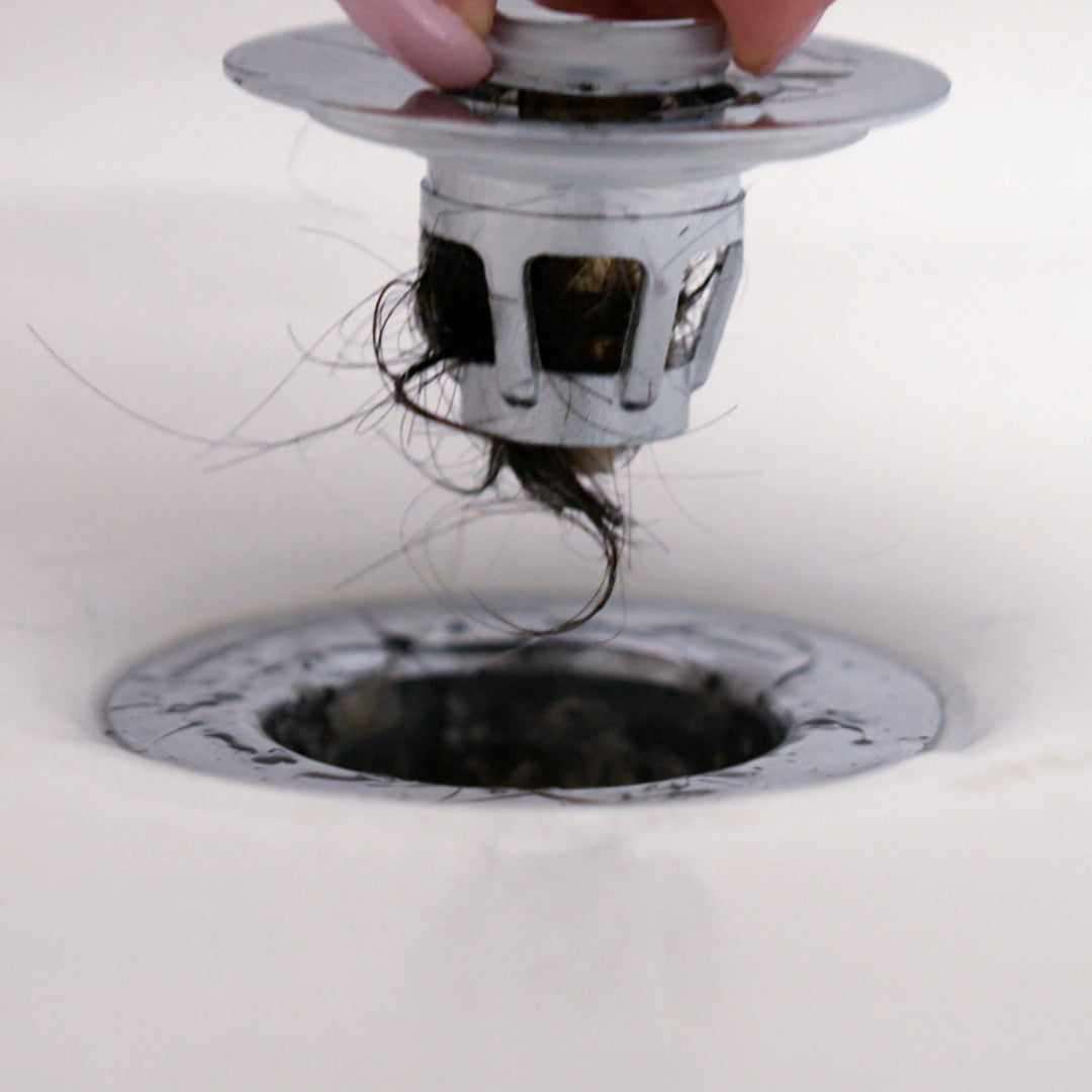 Nahaufnahme eines Drain Magic Abflusssiebs mit aufgefangenen Haaren beim Herausziehen aus dem Waschbecken