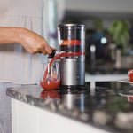 Der Livington JuiceBoost füllt roten Fruchtsaft direkt aus dem Gerät in ein Glas auf der Küchenarbeitsplatte.
