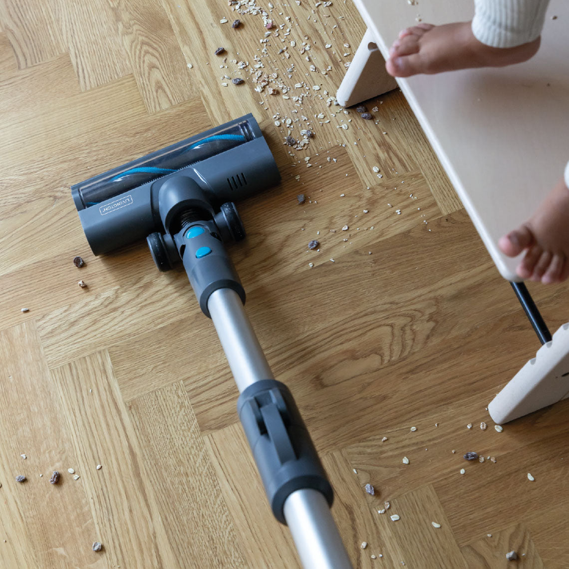 Ein Akkusauger reinigt effektiv verstreute Krümel auf einem Holzfußboden neben einem Kinderstuhl.