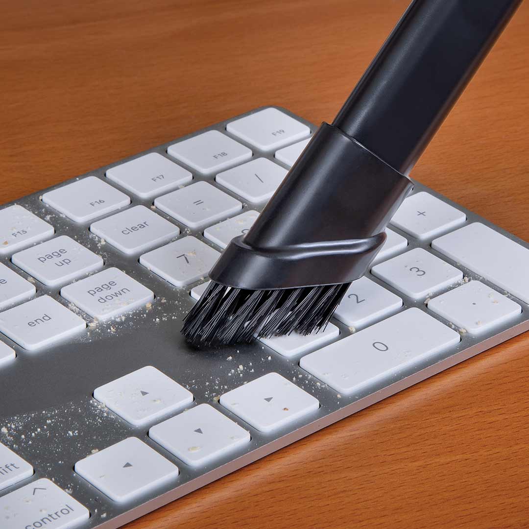 Mit Vac and Blow wird eine Tastatur mit Bürstenaufsatz von Staub und Schmutz zwischen den Tasten gereinigt.