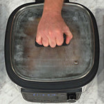 Hand öffnet Glasdeckel des PowerXL Multi Cookers – sichere Handhabung beim Kochen.