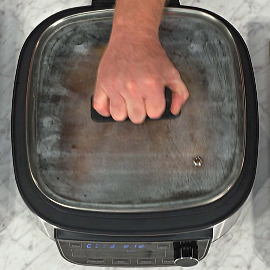 Hand öffnet Glasdeckel des PowerXL Multi Cookers – sichere Handhabung beim Kochen.