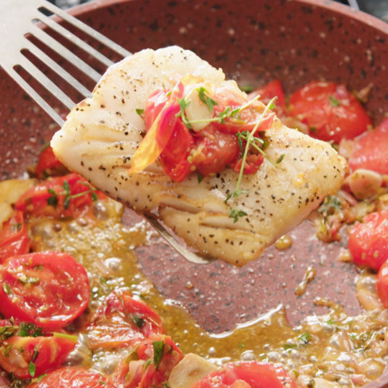 In der Copper and Stone Pan wird ein Stück Fischfilet mit Tomaten und Kräutern zubereitet und mit einem Pfannenwender angehoben.