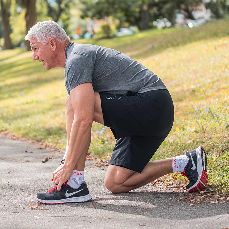 Neuro Socks Athletic – Mann kniet beim Schnüren seiner Schuhe vor dem Lauf, trägt Sportsocken.