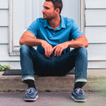 Neuro Socks Wellness – junger Mann sitzt entspannt vor der Tür, trägt schwarze Wellness-Socken.