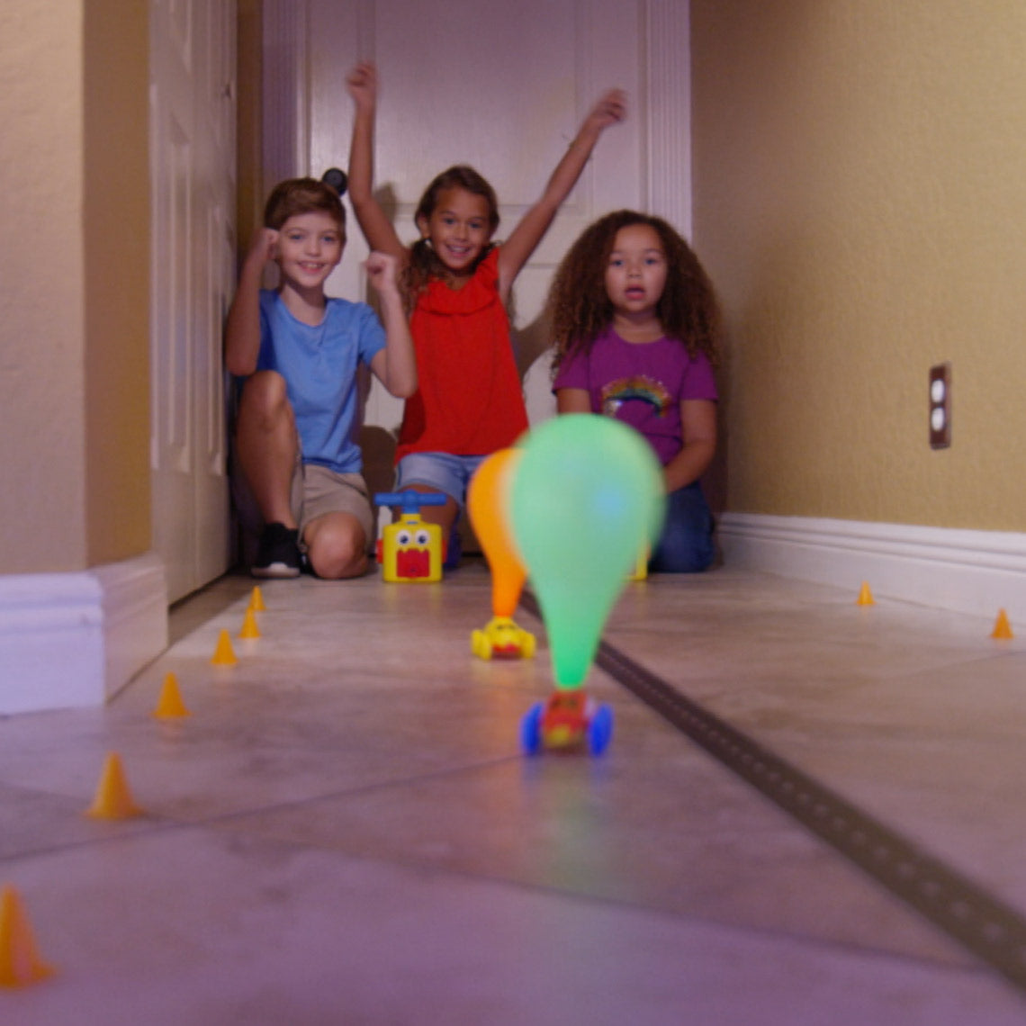 Kinder jubeln, während ein Balloon Zoom Auto mit Ballon-Antrieb durch einen Parcours fährt.