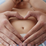 Eltern formen mit den Händen ein Herz auf dem Bauch eines Babys