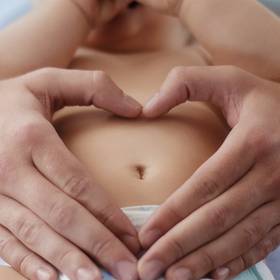 Eltern formen mit den Händen ein Herz auf dem Bauch eines Babys