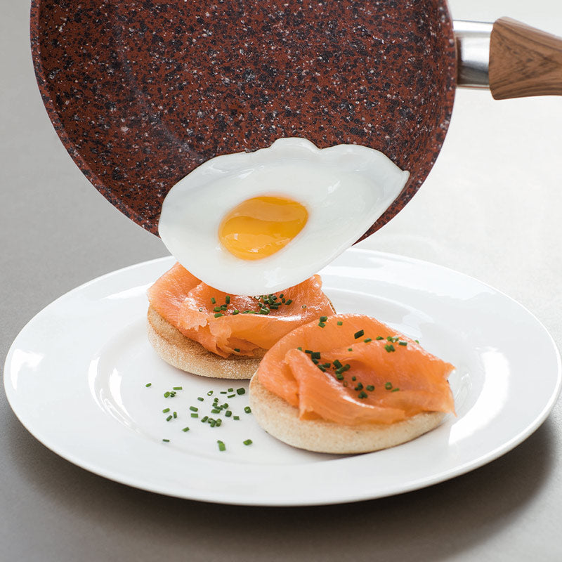 Ein Spiegelei wird aus der Copper and Stone Pan auf ein Brötchen mit Lachs auf einem Teller gelegt.