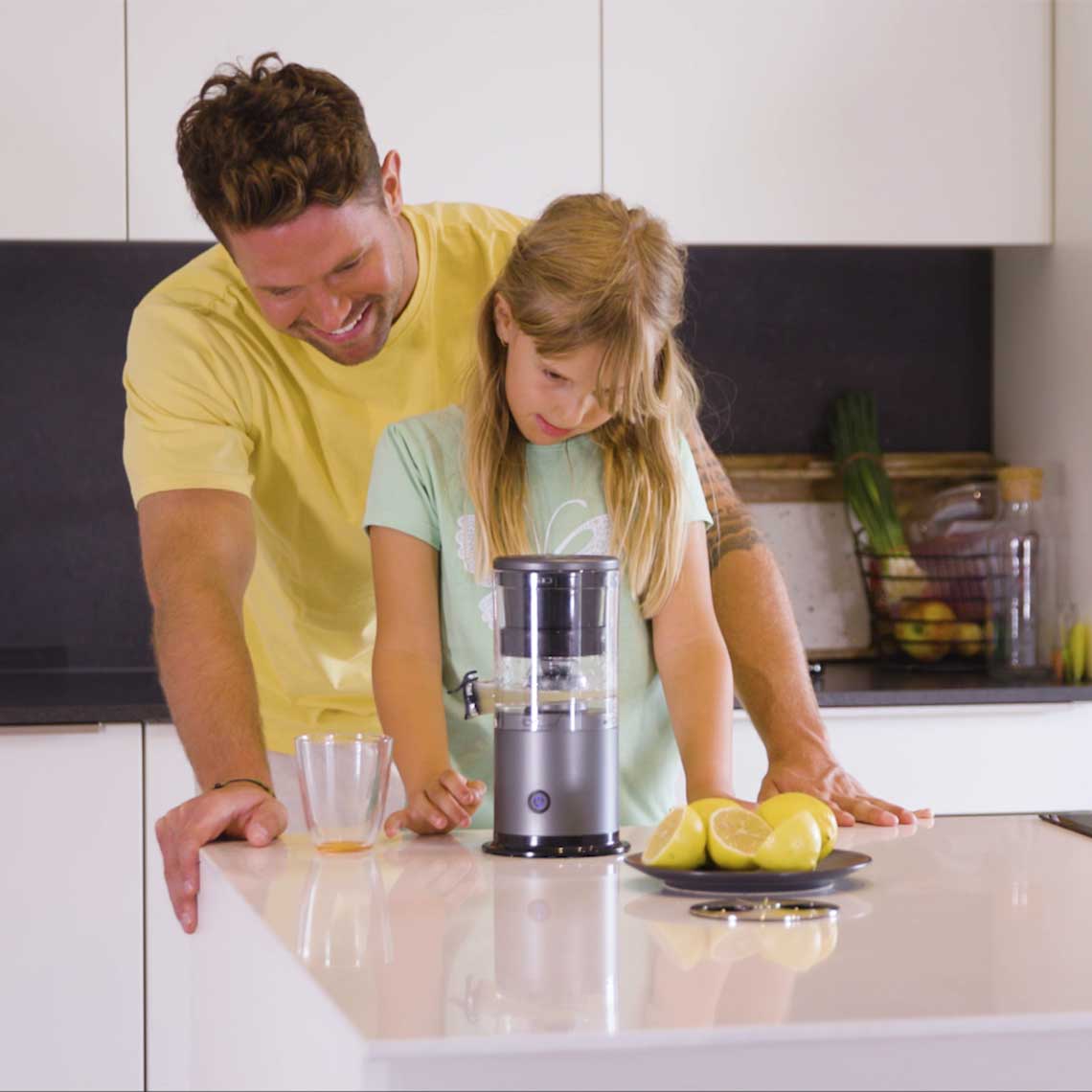 Ein Kind bedient den Livington JuiceBoost in der Küche, daneben steht ein Erwachsener; auf der Theke liegen Zitronen.