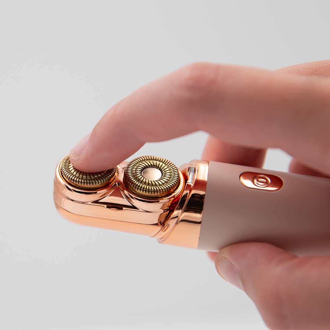 Nahaufnahme von Händen, die ein elegantes elektrisches Gesichts-Beauty-Tool halten; ein Finger berührt den goldfarbenen, rotierenden Aufsatz und die Schnittsicherheit anzudeuten..