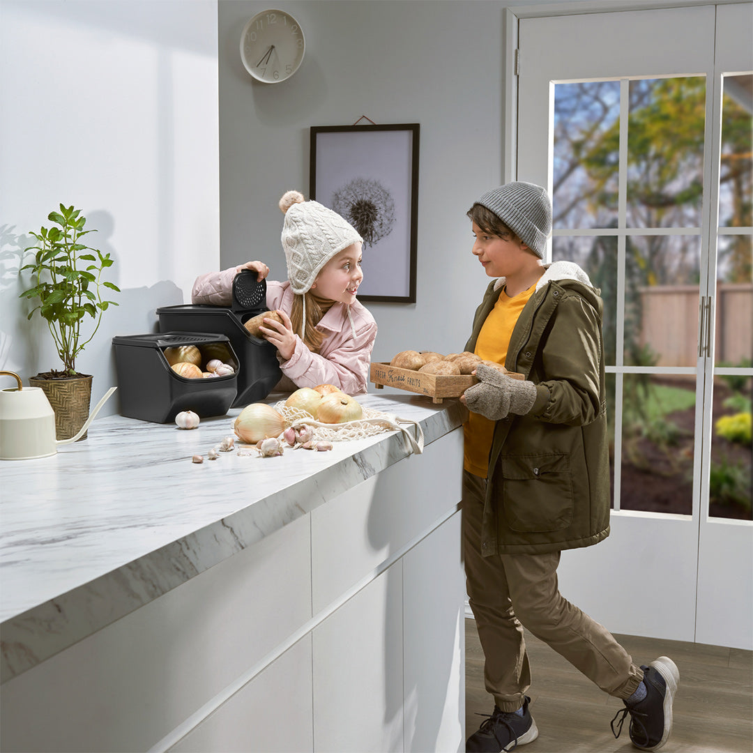 Zwei Kinder in Winterkleidung, eines greift in den Tupperware Potato Smart mit Kartoffeln auf der Küchentheke.