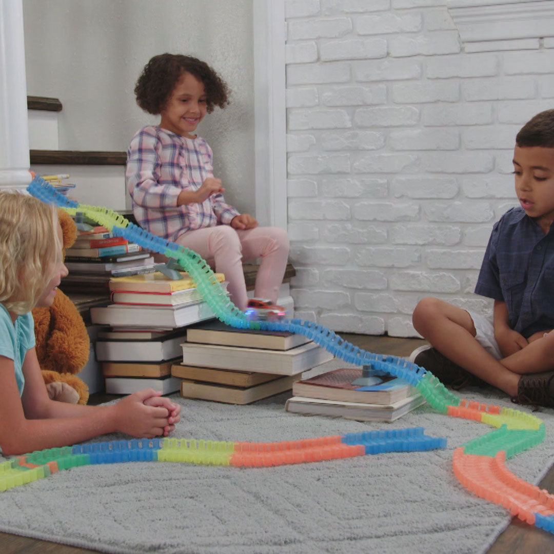 Kinder spielen mit einer Fantastic-Tracks Strecke, die über gestapelte Bücher als Rampe führt
