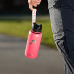 Pinke Trinkflasche mit schwarzem Deckel und Trageschlaufe wird an der Schlaufe neben dem Bein einer Person im Freien gehalten.