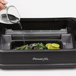 PowerXL Smokeless Grill – Wasser wird in Aromaschale mit Kräutern und Limetten unter der Grillfläche gegossen.