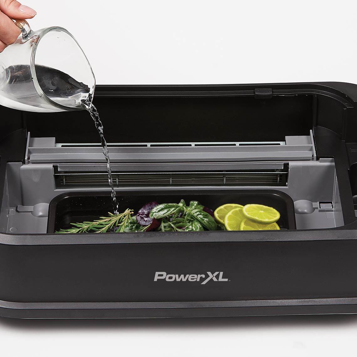 PowerXL Smokeless Grill – Wasser wird in Aromaschale mit Kräutern und Limetten unter der Grillfläche gegossen.