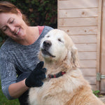Frau pflegt einen Hund mit dem True Touch Handschuh im Garten – der Hund wirkt entspannt.