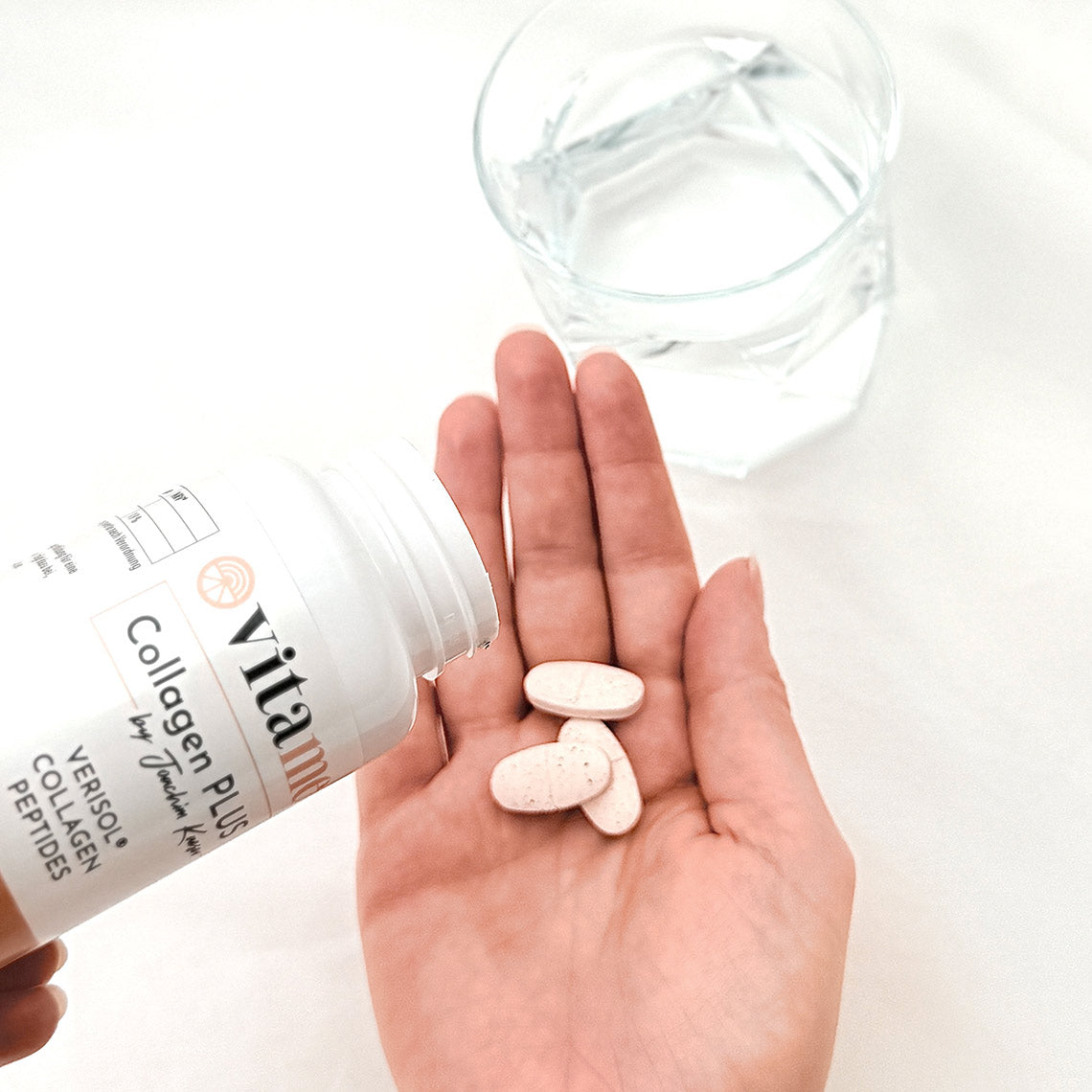 Eine Hand hält mehrere Tabletten, daneben eine geöffnete „Collagen Plus“-Flasche und ein Glas Wasser.