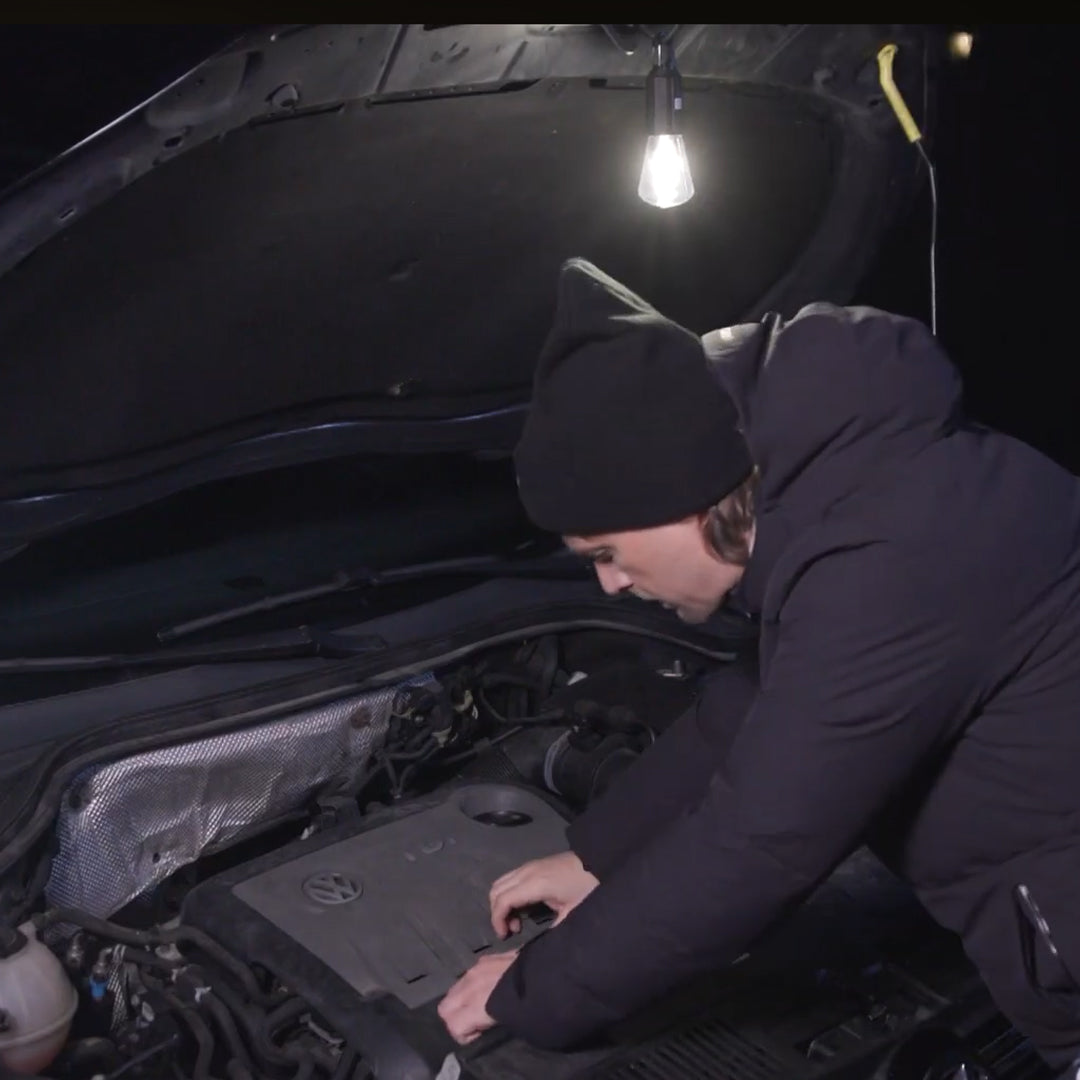 Person arbeitet bei Nacht am Motorraum mit aufgehängter LED-Leuchte