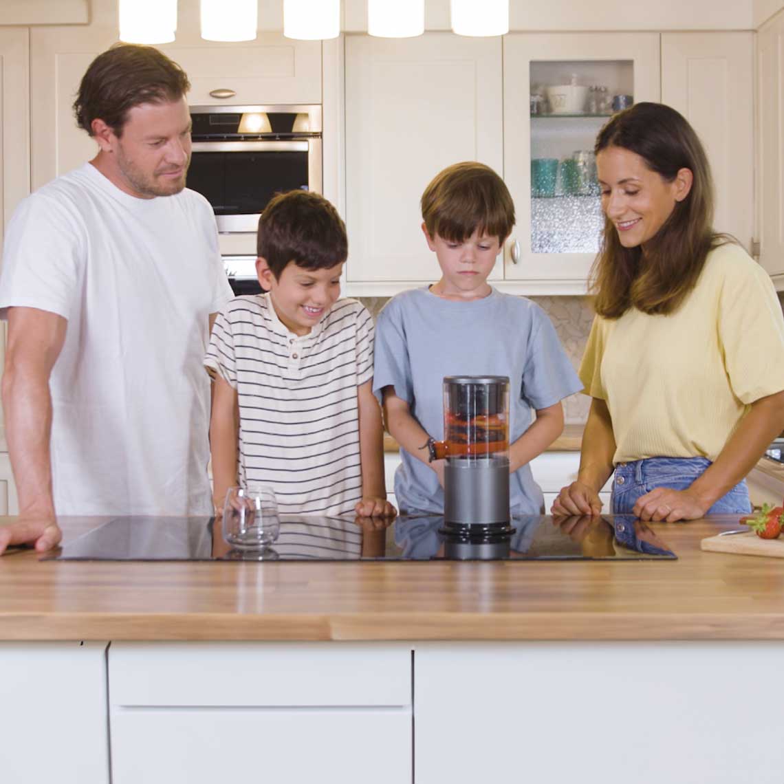 Eine Familie steht in der Küche um den eingeschalteten Livington JuiceBoost, ein Glas steht daneben auf der Arbeitsfläche.