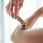 Hand führt ein elektrisches Beauty-Rasiergerät mit goldfarbenem Aufsatz über den angewinkelten Ellenbogen und rasiert den Unterarm.