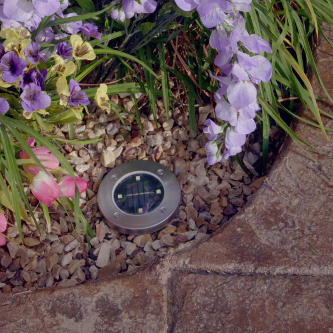 Solar-LED-Bodenleuchte im Blumenbeet bei Tag.