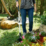 Mit dem Hammersmith Bionic Trimmer kürzt eine Person das Gras präzise an Blumenbeeten im Garten.