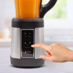 Nahaufnahme des Livington Revolution Blender mit gefülltem Behälter; eine Hand berührt das Bedienfeld, um den Mixvorgang zu starten.