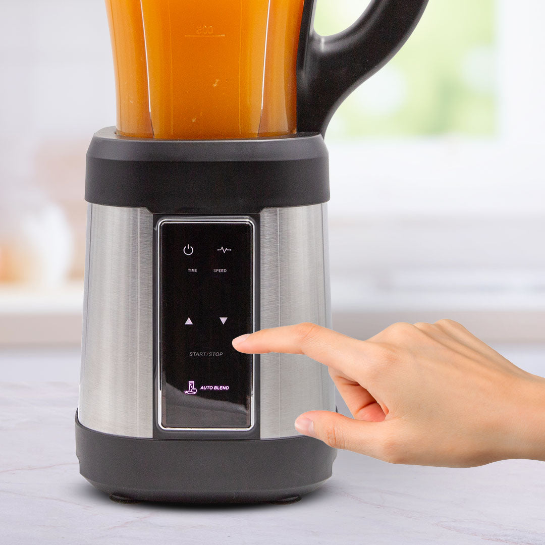 Nahaufnahme des Livington Revolution Blender mit gefülltem Behälter; eine Hand berührt das Bedienfeld, um den Mixvorgang zu starten.