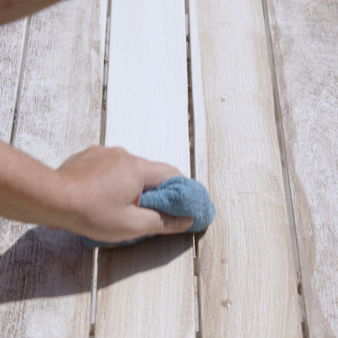 Mit Magic Shine reinigt eine Hand mit einem blauen Tuch eine Holzoberfläche – sauberer, heller Bereich links, schmutzig und dunkel rechts