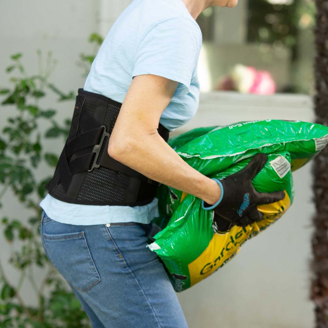 Person trägt den Copper Fit X Belt beim Heben eines schweren Gegenstands im Garten