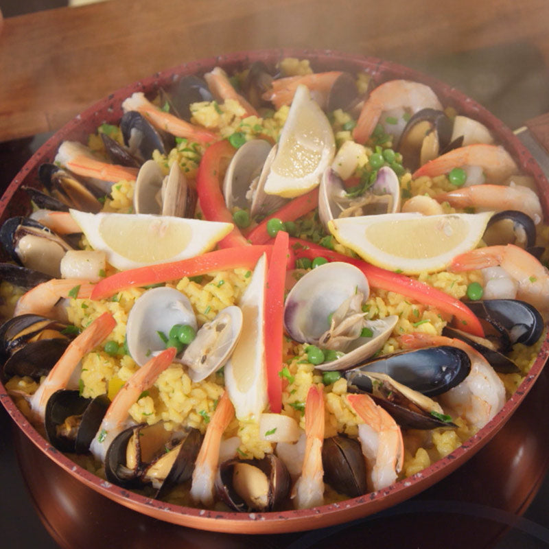 In der Copper and Stone Pan wird eine Paella mit Meeresfrüchten, Erbsen, Paprika und Zitronenspalten zubereitet.
