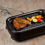 PowerXL Smokeless Grill – gegrilltes Steak mit Gemüse auf Grillplatte, Glasdeckel liegt seitlich.