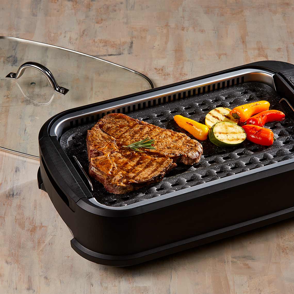 PowerXL Smokeless Grill – gegrilltes Steak mit Gemüse auf Grillplatte, Glasdeckel liegt seitlich.
