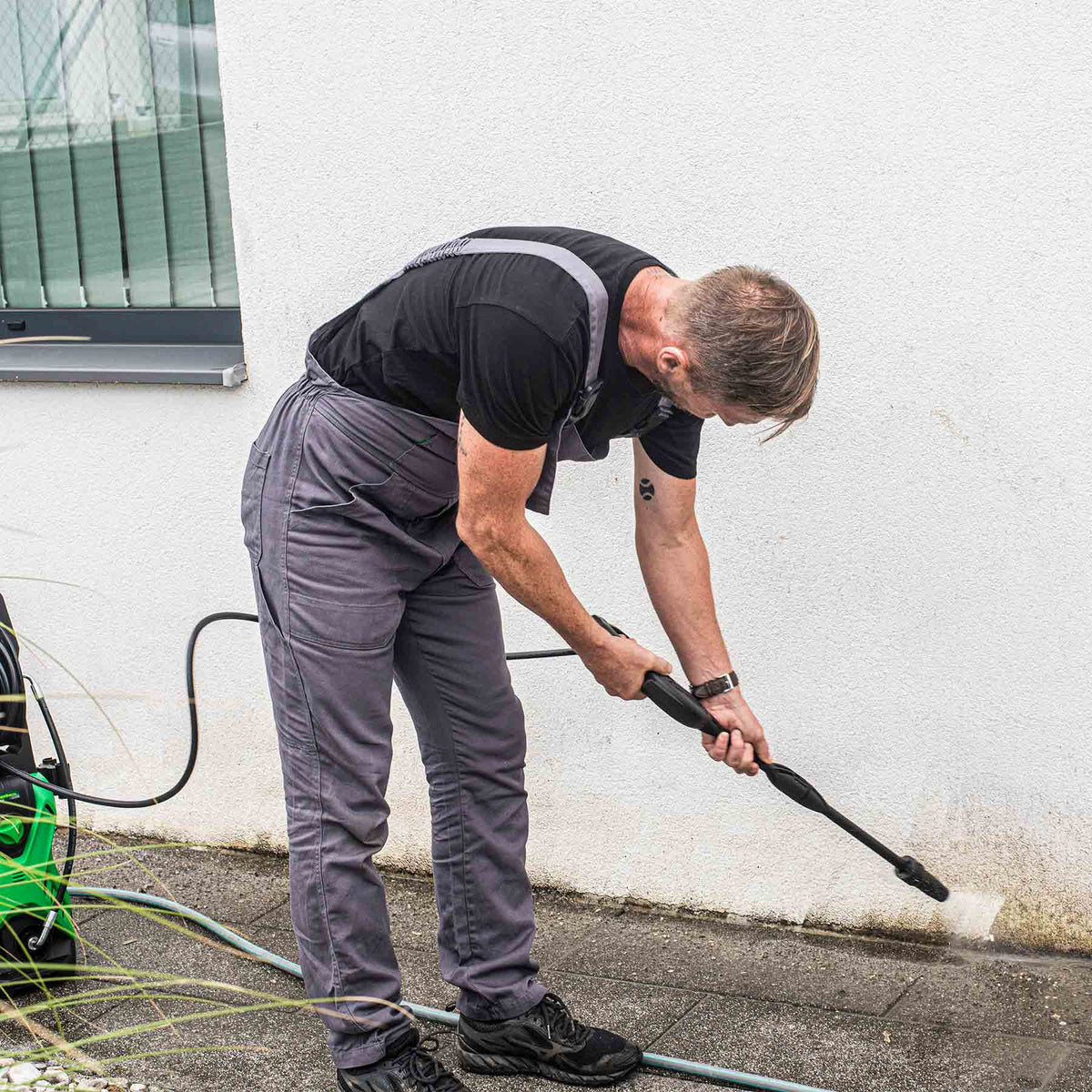 Mann entfernt hartnäckigen Schmutz von einer Hauswand mit dem Hammersmith ProJet Hochdruckreiniger.