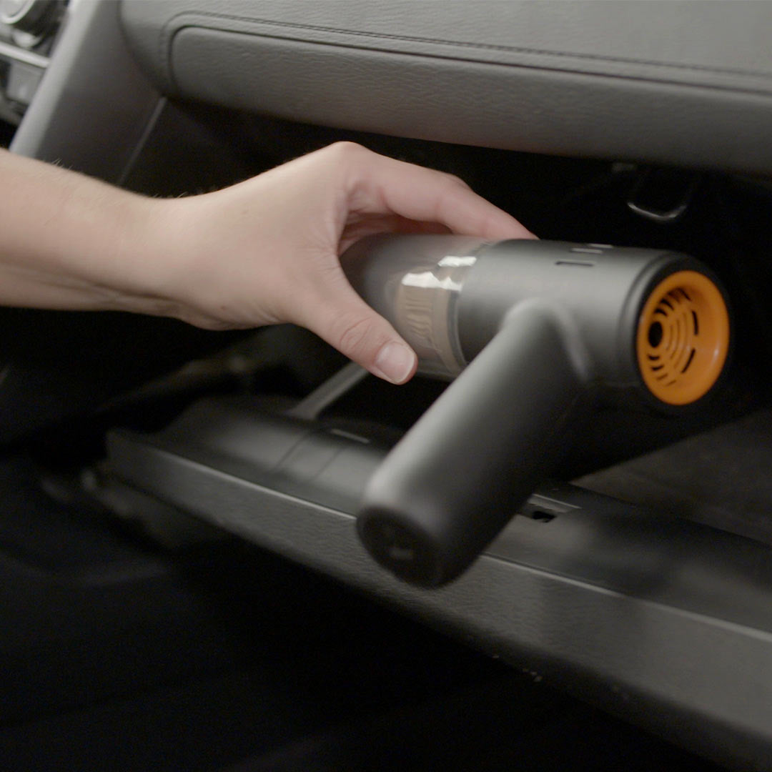 Ein Handstaubsauger wird im Auto unter dem Handschuhfach verwendet – ideal für schwer erreichbare Stellen im Innenraum.