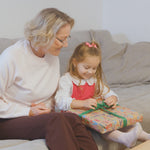Mädchen öffnet ein Geschenk neben einer älteren Frau auf dem Sofa.