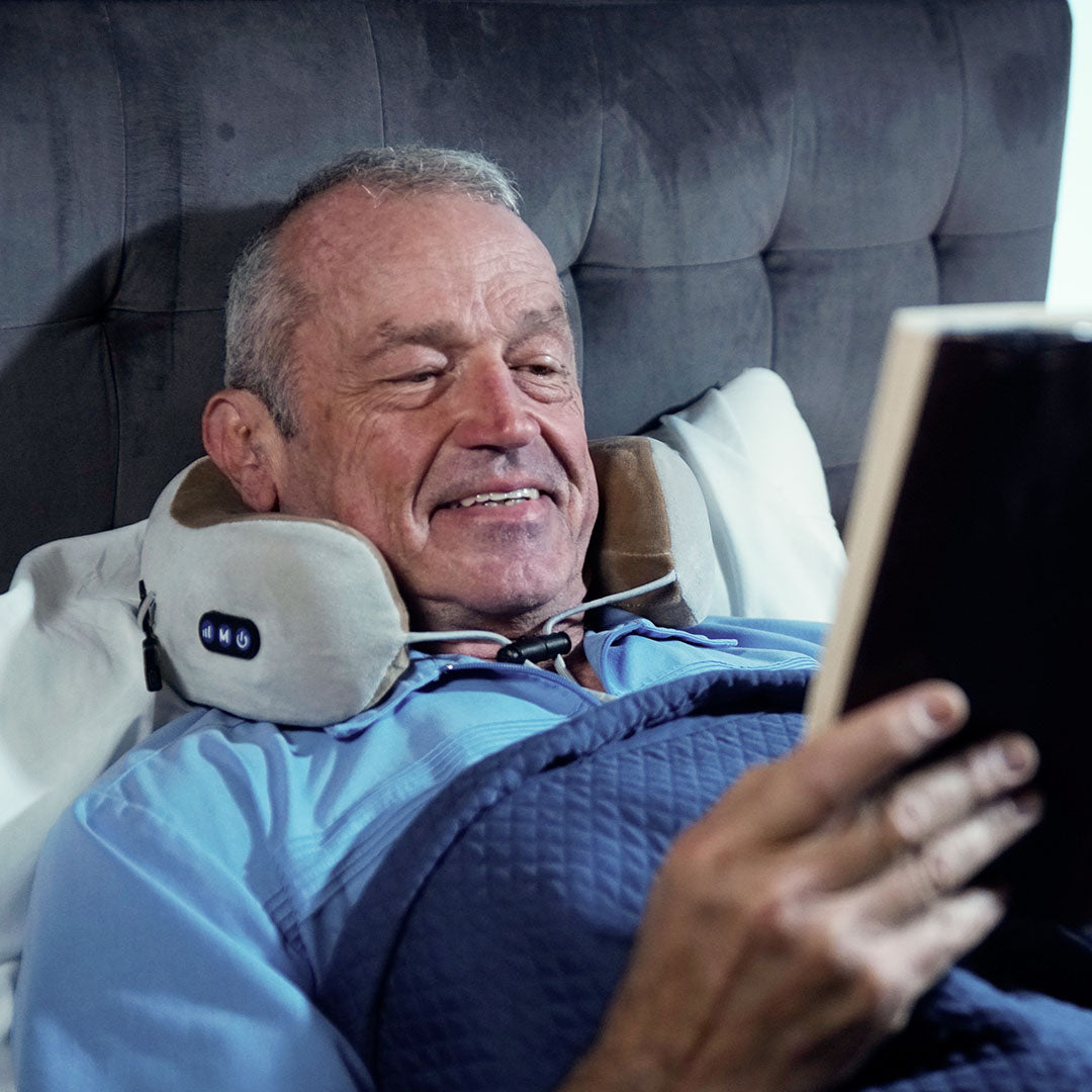 Mann liegt mit dem Nackenmassagegerät im Bett und liest Buch