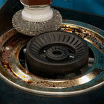 Metallbürste reinigt gründlich einen stark verschmutzten Gasherd-Brenner.