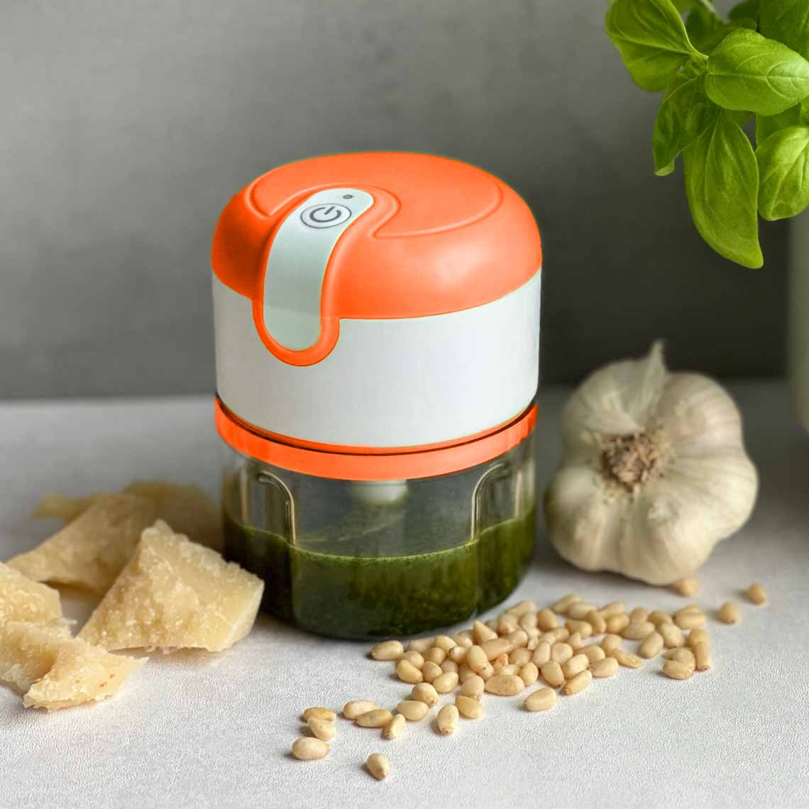 Kleiner elektrischer Zerkleinerer mit orangenem Deckel, ideal für Pesto mit Käse, Knoblauch und Pinienkernen.