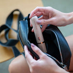 Eine Frau legt ein kompaktes elektrisches Beauty-Gerät in eine kleine Handtasche – ideal für die Anwendung unterwegs.