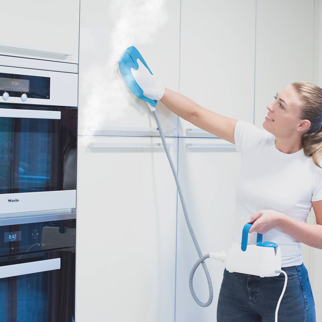 Eine Frau reinigt Küchenschränke mit heißem Dampf durch den Livington SteamTouch.